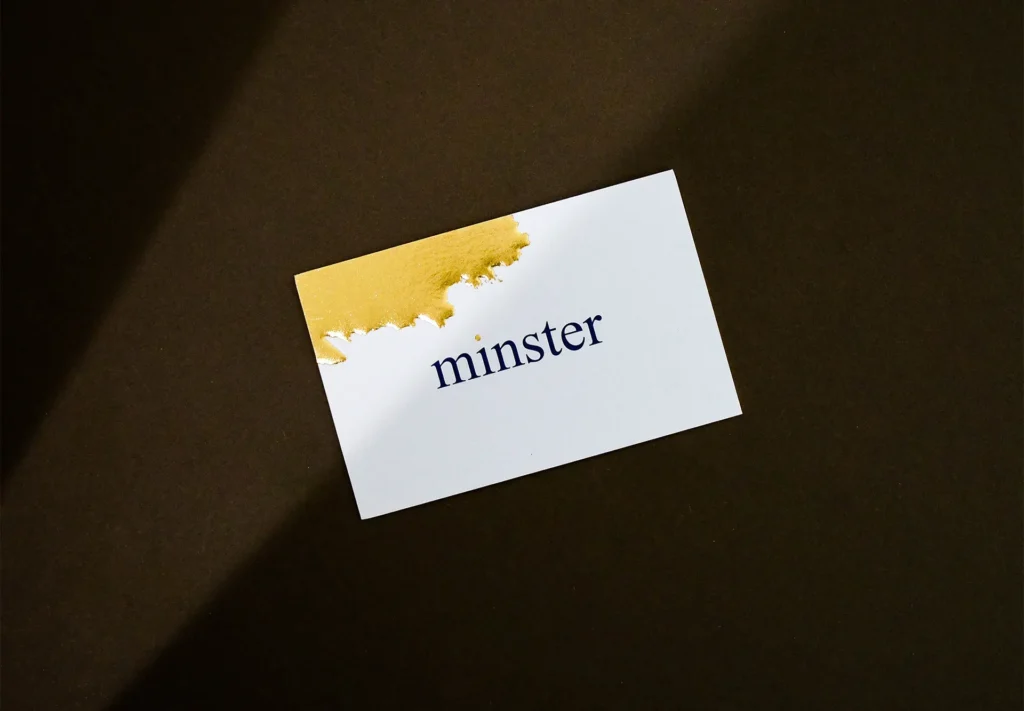 A sleek white business card with a gold paint blob elegantly printed in gold foil at the top left corner, adding a touch of creativity.