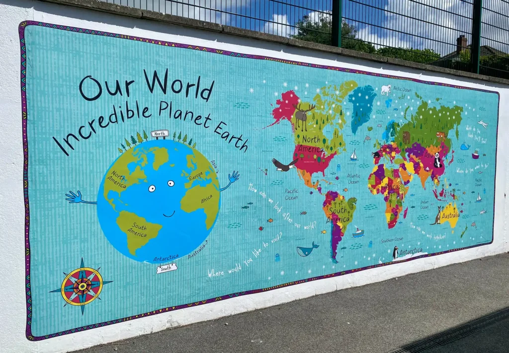 A large bright and colourful vinyl mural of the world on a school playground wall.