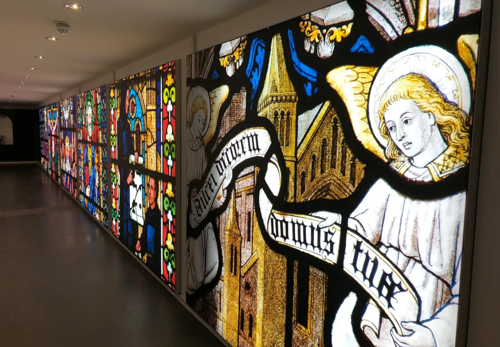 Large wall display of backlit prints featuring intricate stained glass window designs, illuminated to showcase vibrant colours and detailed patterns, creating a stunning visual effect.