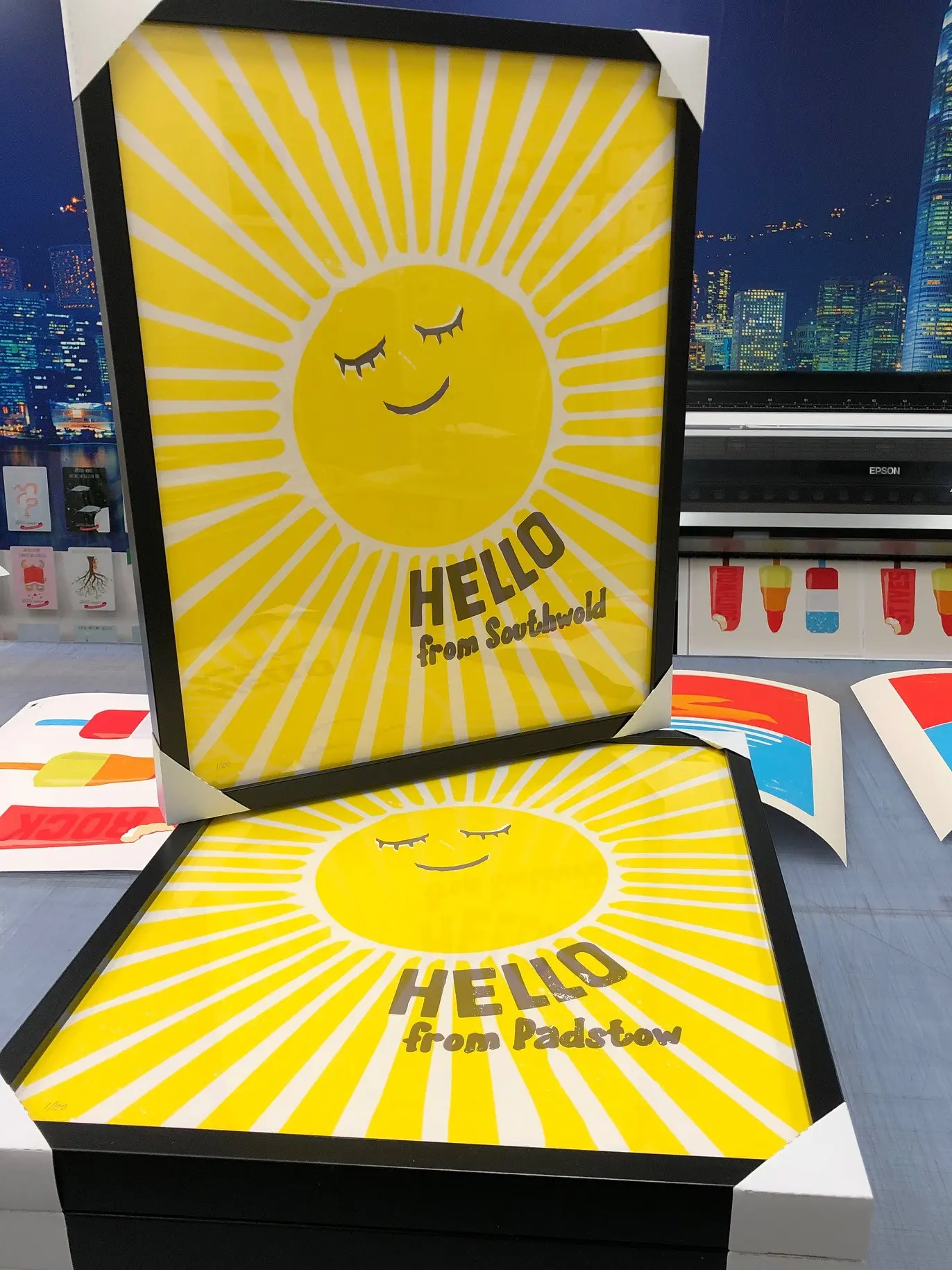 A framed poster featuring an illustration of a large sun with a smily face and the text Hello from Southwold.