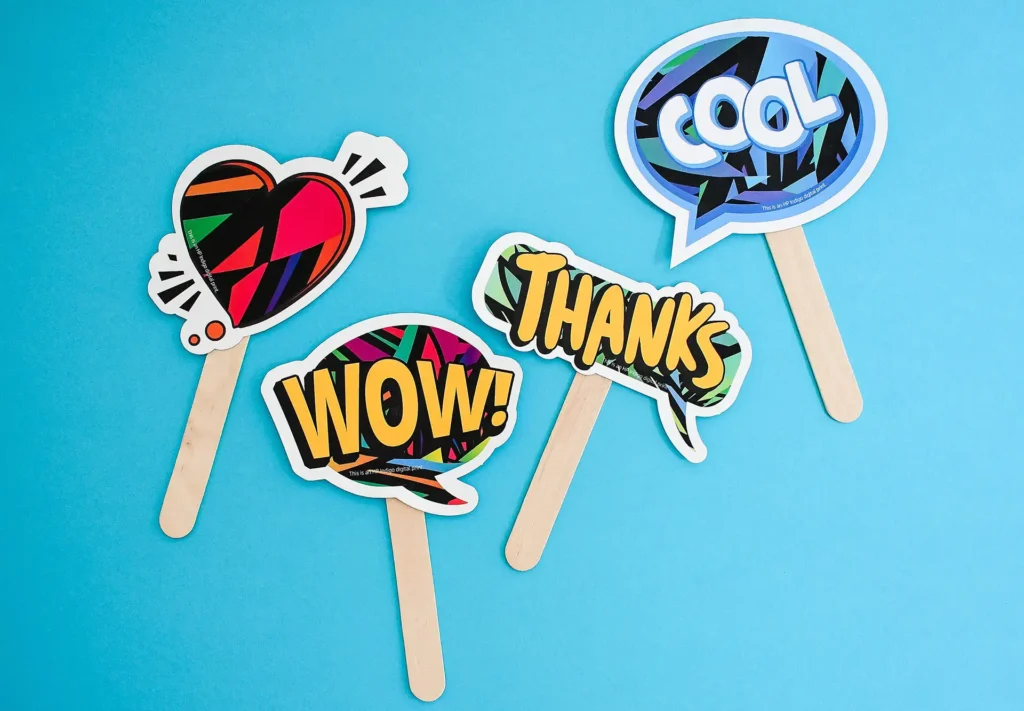 A creative collection of pop-art inspired signs mounted on popsicle sticks, featuring fun words like 'wow' and 'thanks'.